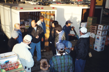 people conversing around a truck with boxes of produce